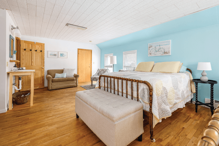 A bedroom with a blue accent wall, featuring a queen bed, a bench, a sofa, and wooden furniture.