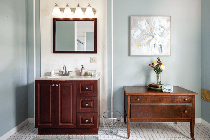 A bathroom with a dark wood vanity, a mirror, a table, and artwork on the wall.