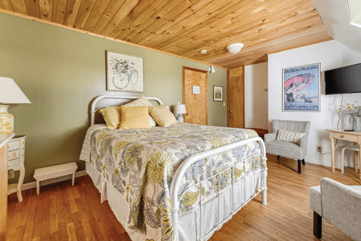 A bedroom featuring a white metal bed with a floral patterned quilt, a wood plank ceiling, and green walls.