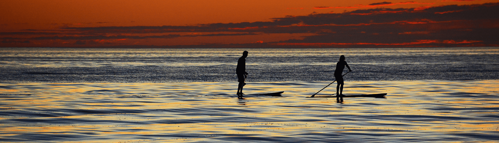 Two silhouetted paddleboarders gliding over a serene ocean at sunset.