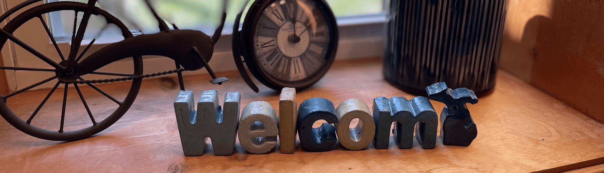 A wooden "Welcome" sign surrounded by a clock and a decorative bicycle wheel.
