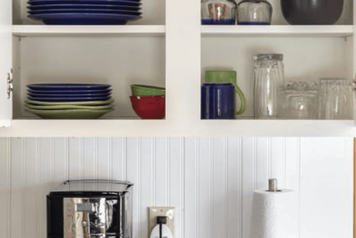 A close-up of white kitchen cabinets with dishes, glasses, and a coffee maker.