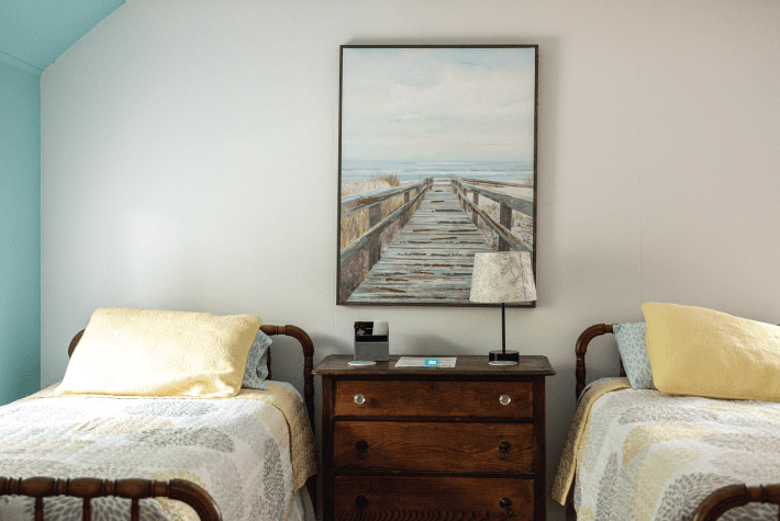 A bedroom with two twin beds, a wooden dresser, and a framed painting of a pier.