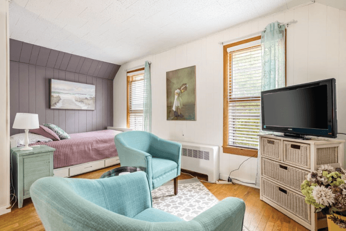 A bedroom with two robin egg blue armchairs, a TV on a bureau, a bed in the background, and artwork on the walls.