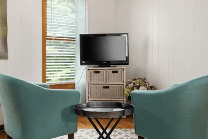 A room with two robin egg blue upholstered armchairs, a flat-screen TV on a dresser, and a round wooden table between them.