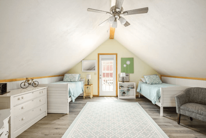 An attic bedroom with two twin beds, a sloped ceiling, and a ceiling fan.