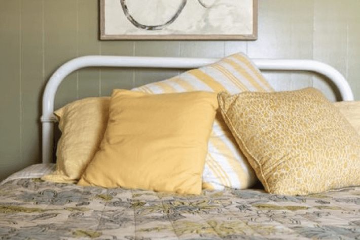 A close-up of a white metal bed with yellow pillows and a patterned quilt.