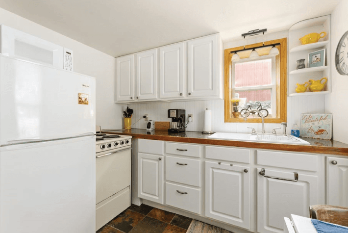 A kitchen with white cabinets, white appliances, a wooden countertop, and a window with a yellow curtain.