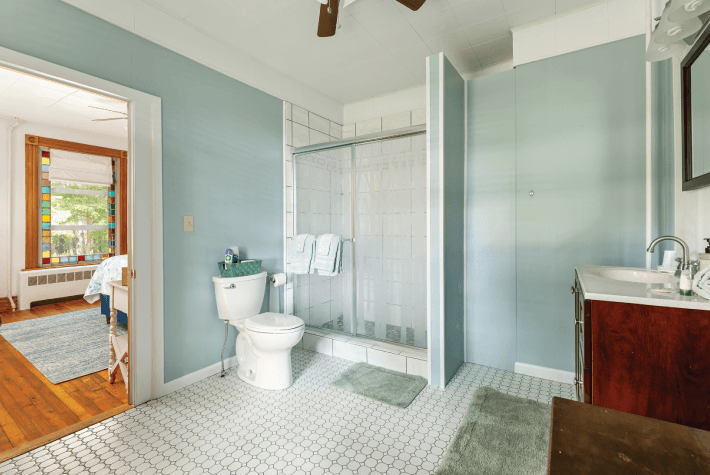 A large bathroom featuring a shower with a curtain, a toilet, a vanity sink, and a doorway leading to another room.