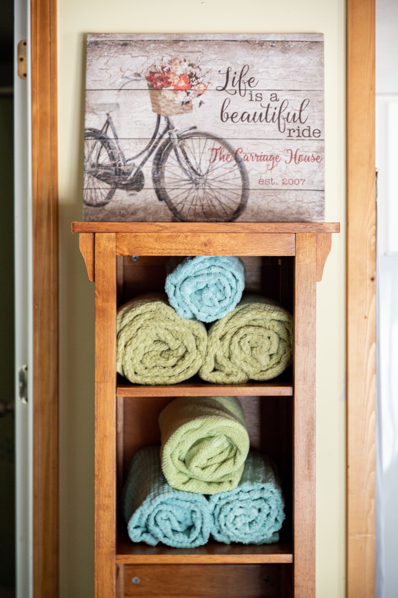 A wooden shelf with rolled towels and a framed picture of a bicycle above.